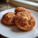 Three freshly baked churro cookies generously coated in cinnamon sugar, resting on a white plate.