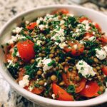 Close-up of a vibrant lentil salad mixed with halved cherry tomatoes, feta cheese, and fresh parsley.