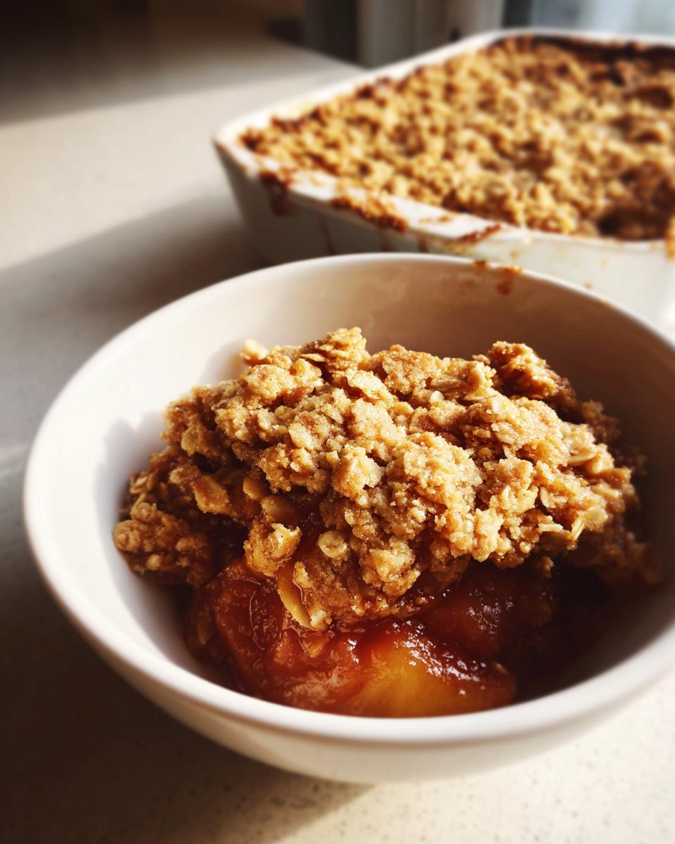 Close-up of a serving of amazing peach crisp with a thick, crunchy topping in a white bowl.