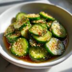 Close-up of sliced cucumbers marinated in a savory dressing and topped with toasted sesame seeds for asian cucumber salad.