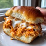 A close-up view of one of the buffalo chicken sliders, featuring shredded orange buffalo chicken topped with white ranch or blue cheese dressing on a soft roll.