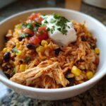 A close-up of a white bowl filled with a delicious chicken burrito bowl featuring seasoned rice, shredded chicken, corn, and black beans.