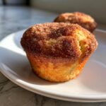 A close-up of a golden brown cinnamon sugar french toast muffins topped with sparkling sugar crystals.