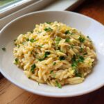 Close-up of creamy lemon orzo pasta topped with fresh parsley and lemon zest in a white bowl.