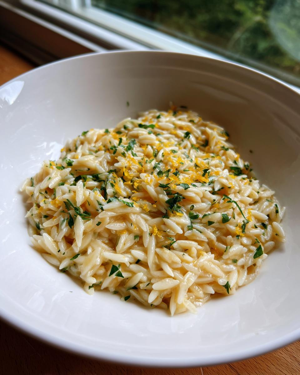 Close-up of creamy lemon orzo pasta topped with fresh parsley and bright yellow lemon zest.