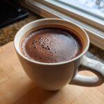 Close-up of a white mug filled with rich, dark crockpot hot chocolate topped with small bubbles.