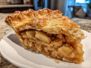 Close-up of a thick slice of homemade apple pie showing a flaky, golden crust and chunky cinnamon-spiced apple filling.
