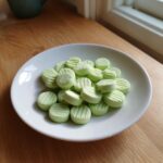 A pile of light green, round cream cheese mints with ridged tops, served on a small white plate.
