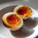 Close-up of a marinated egg cut in half showing a perfectly jammy, bright orange yolk.