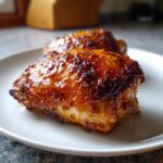 Close-up of a perfectly glazed, caramelized, and juicy chicken thighs on a white plate.