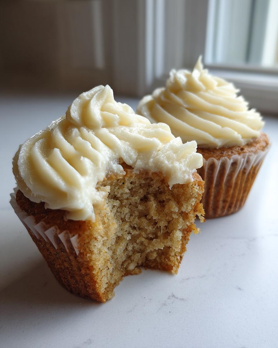Close-up of a banana cupcakes with a bite taken out, showing the moist crumb and thick cream cheese frosting.