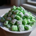 A mound of bright green, powdered sugar-dusted pistachio puppy chow piled high on a white plate.