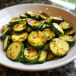Close-up of golden brown, seasoned sauteed zucchini slices piled high in a white bowl.
