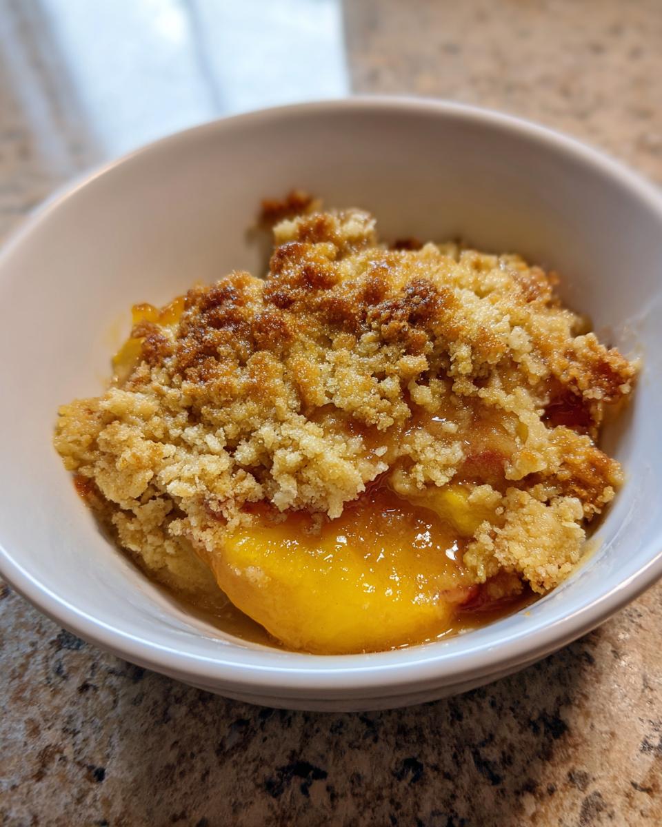 Close-up of a serving of warm peach crisp with golden brown topping in a white bowl.
