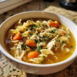 Close-up of a hearty bowl of slow cooker chicken noodle soup, featuring shredded chicken, egg noodles, and sliced carrots.