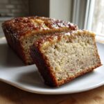 A slice cut from a loaf of moist snickerdoodle banana bread with a glossy, caramelized top.