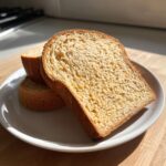 Close-up of three slices of soft, golden brown whole wheat bread stacked on a white plate.