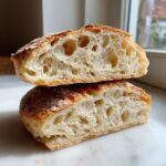 Close-up of two halves of a sourdough english muffin stacked, showing the open, airy crumb structure.