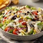 Close-up of a hearty southwest salad featuring shredded chicken, avocado, black beans, corn, tomatoes, and creamy dressing.