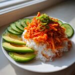 A close-up of a spicy crab sushi bowl featuring bright orange spicy crab mix over white rice, served with sliced avocado and cucumber.