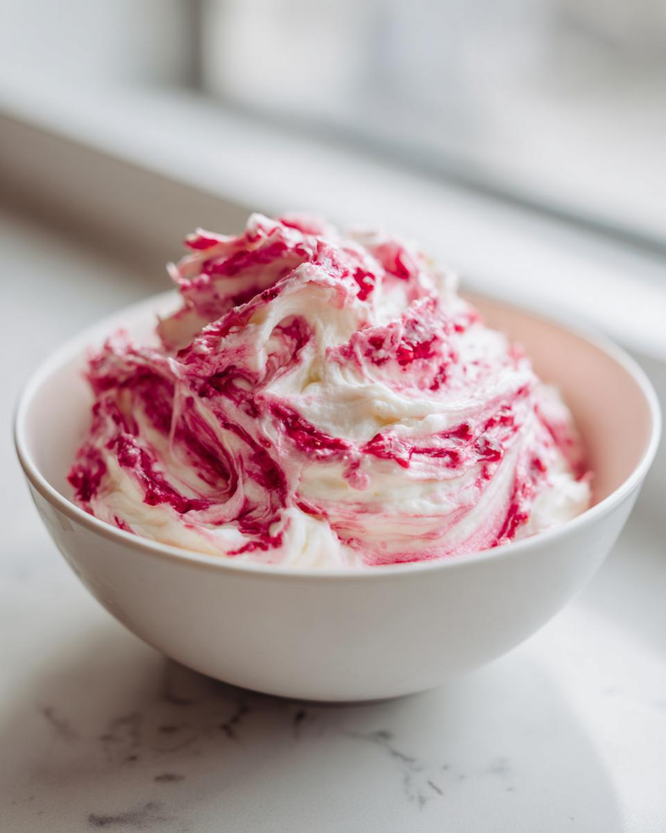 Close-up of creamy strawberry cheesecake dip swirled with bright pink fruit puree in a white bowl.