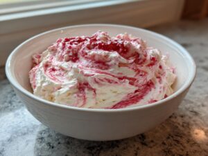 Close-up of creamy strawberry cheesecake dip swirled with red strawberry sauce in a white bowl.