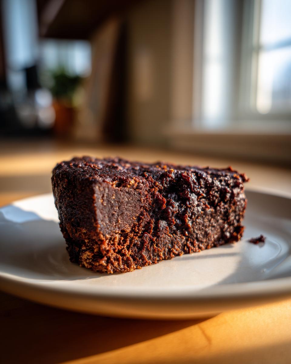 Close-up of a dense, dark brown, sturdy black bean burger patty slice on a white plate.