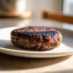 Close-up of a thick, well-seared black bean burger patty resting on a light-colored plate.