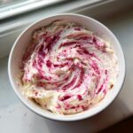 Close-up of creamy white mixture swirled with bright pink strawberry puree, ready to serve as strawberry cheesecake dip.
