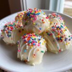 Close-up of several white chocolate sugar cookie truffles topped with colorful sprinkles.