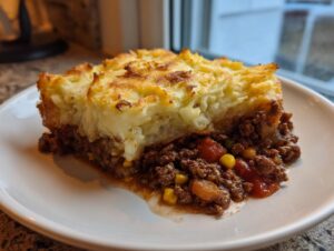 A hearty slice of amazing cottage pie featuring a thick, browned mashed potato topping over a rich ground meat and vegetable filling.