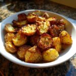 A white bowl filled with perfectly crispy, golden brown roasted potatoes seasoned with herbs.