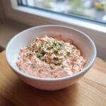A white bowl filled with creamy, pink smoked salmon dip, garnished generously with fresh dill.