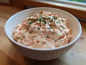A white bowl filled with creamy, pink smoked salmon dip, garnished with fresh dill.