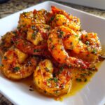 A close-up of perfectly cooked cajun shrimp coated in a rich, buttery sauce with visible herbs and spices.