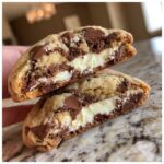 Close-up of a chocolate chip cheesecake cookie cut in half, showing the creamy cheesecake filling and melted chocolate chips.