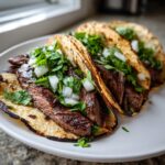 Three delicious steak tacos filled with sliced grilled steak, topped with fresh diced white onion and cilantro.