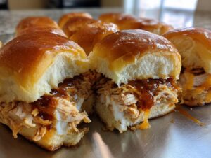 Close-up of two delicious bbq chicken sliders filled with shredded chicken, BBQ sauce, and melted cheese on shiny buns.