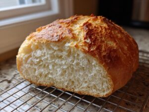 A loaf of homemade yeast bread, cut in half to show the fluffy white interior and golden crust, resting on a cooling rack.