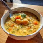 A spoonful of thick greek chickpea soup, showing chickpeas, carrots, and fresh dill, lifted from a white bowl.