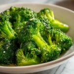 Close-up of bright green, perfectly steamed broccoli florets seasoned with salt and pepper in a white bowl.